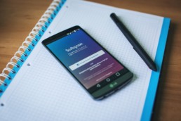 Smartphone con instagram aperto appoggiato su un quaderno e con accanto una penna